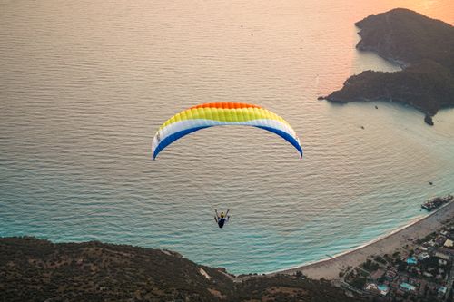 Free A colorful paraglider soaring over a picturesque coastline during sunset, capturing the thrill of adventure sports with a serene backdrop. Stock Photo