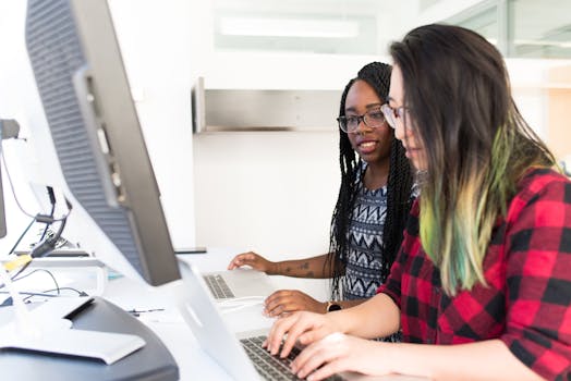 Two women working together on laptops in a bright, modern office space.