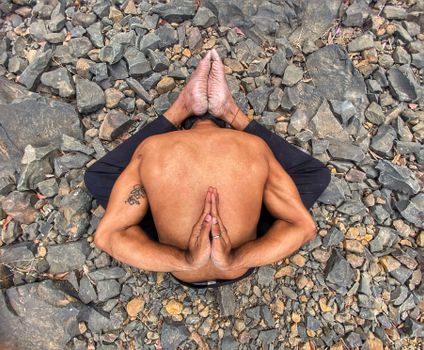 A man performs a complex yoga pose on rocky ground, showcasing strength and flexibility.
