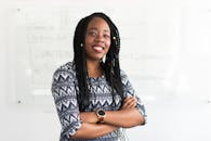 一名年轻女子自信地交叉双臂微笑着，站在一间明亮的现代化办公室里