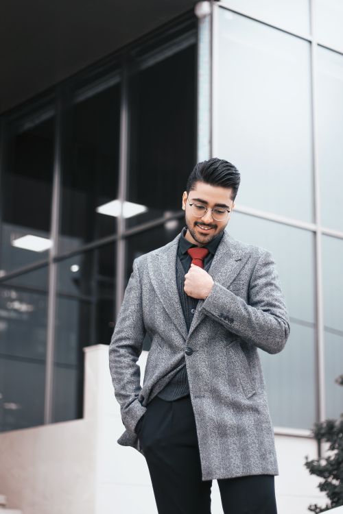 Free A fashionable man adjusts his red necktie in a modern urban environment. Stock Photo