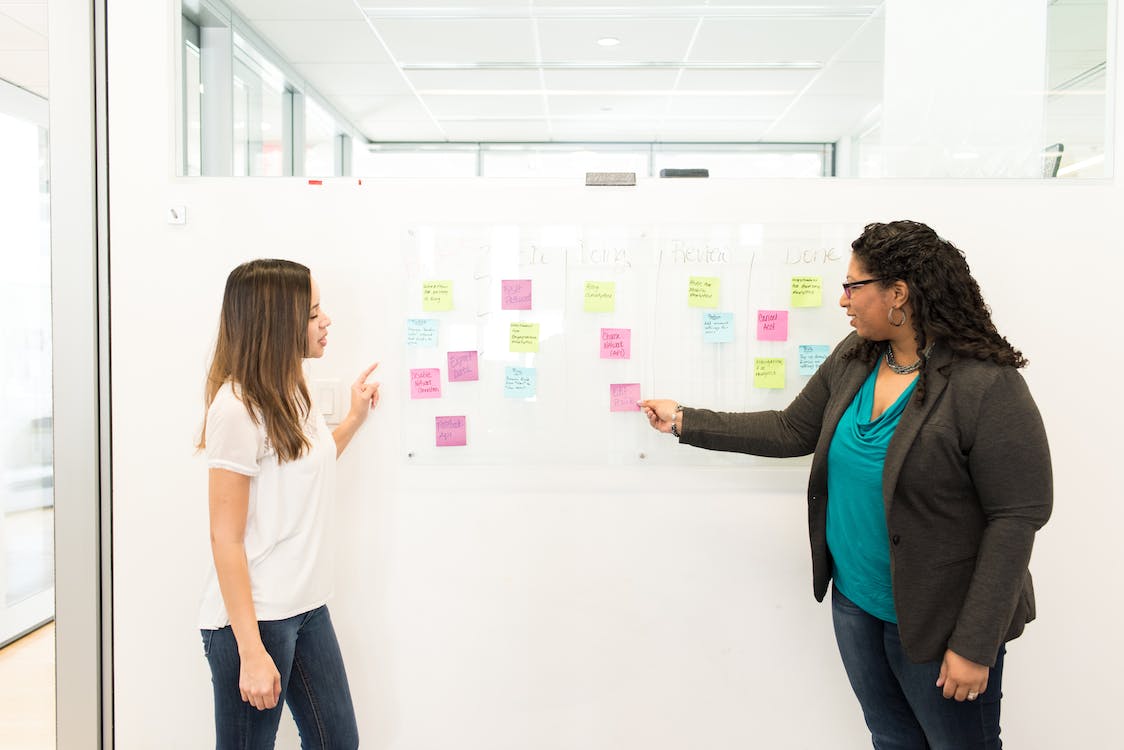 two people standing in front of a white board with colorful sticky notes