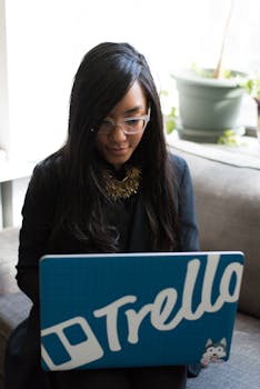 Focused woman using a laptop with Trello branding in a cozy indoor setting.