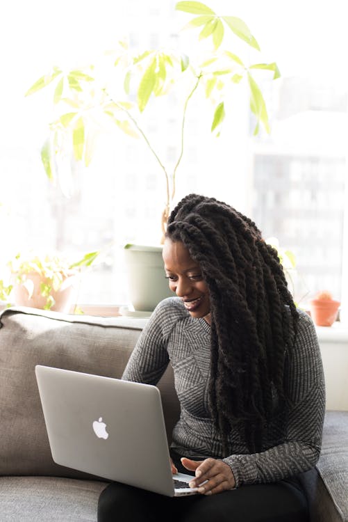 Free Woman Sittin on Gray Couch While Holding Her Apple Macbook Air Stock Photo