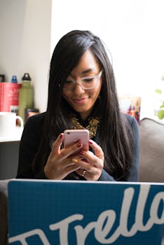 A happy woman with glasses checking her phone indoors, using Trello.