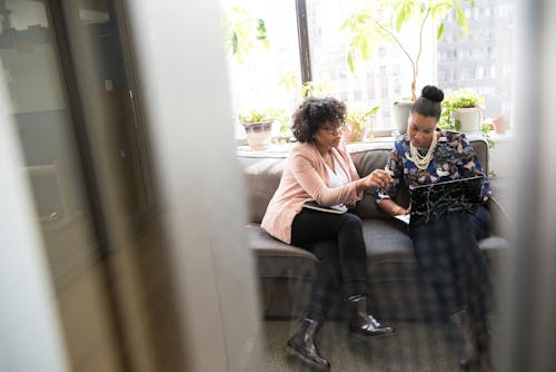 Free Shallow Focus Photography of Two Woman Sitting on Gray Couch Stock Photo