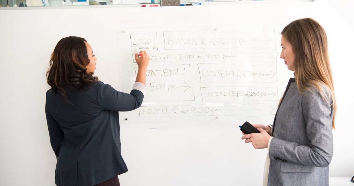 Two women discussing an office presentation at a whiteboard.