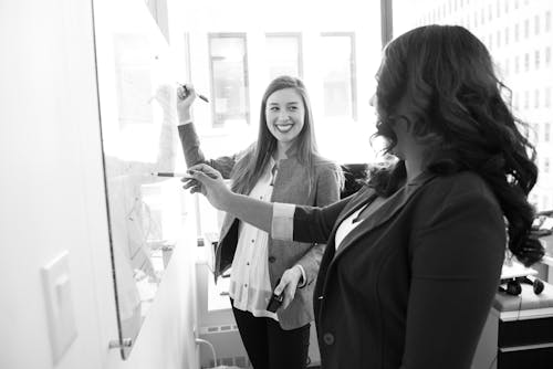 Two Smiling Woman Writing on Board