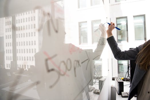 Business professional writing on a whiteboard in a bright office setting, showcasing modern work dynamics.