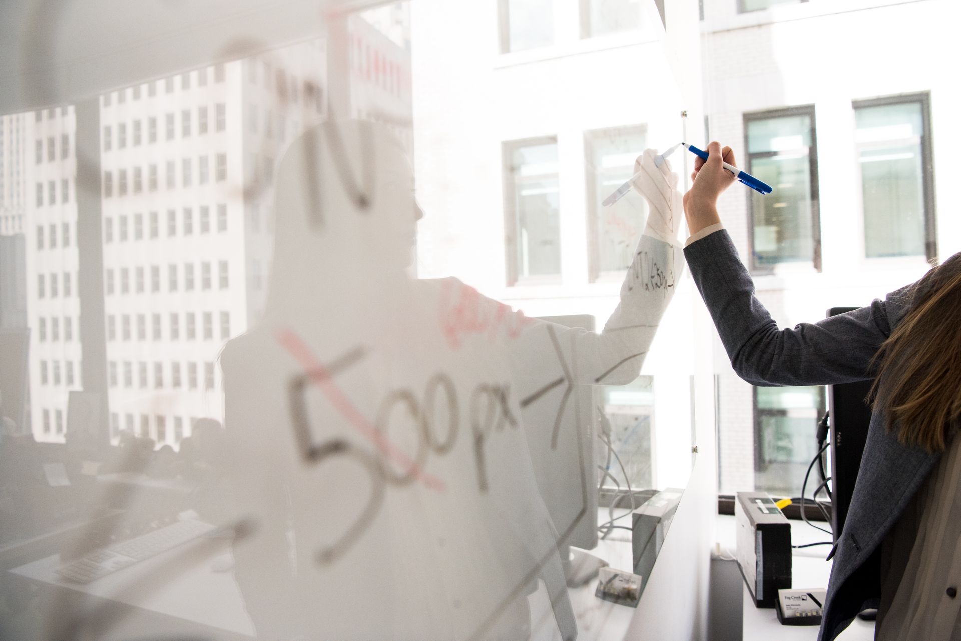 Business professional writing on a whiteboard in a bright office setting, showcasing modern work dynamics.