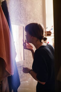A woman standing by a mirror applying makeup in a warmly lit room, creating a cozy atmosphere.