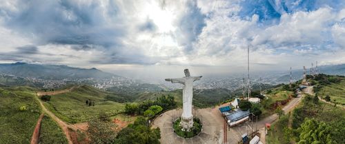 Free A panoramic aerial view of a grand Christ statue on a hilltop, overlooking a vast city and lush green hills. Stock Photo