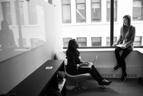 Grayscale Photo of Woman Talking to Her Colleague