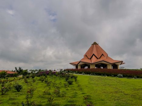 Modern building with a unique roof design surrounded by lush greenery under an overcast sky.