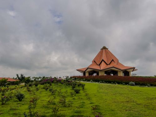 Free Modern building with a unique roof design surrounded by lush greenery under an overcast sky. Stock Photo