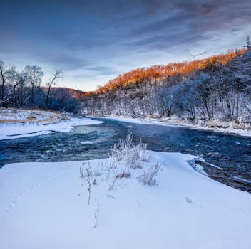 Tranquil winter scene of a river winding through snow-covered hills in Minnesota at sunset.