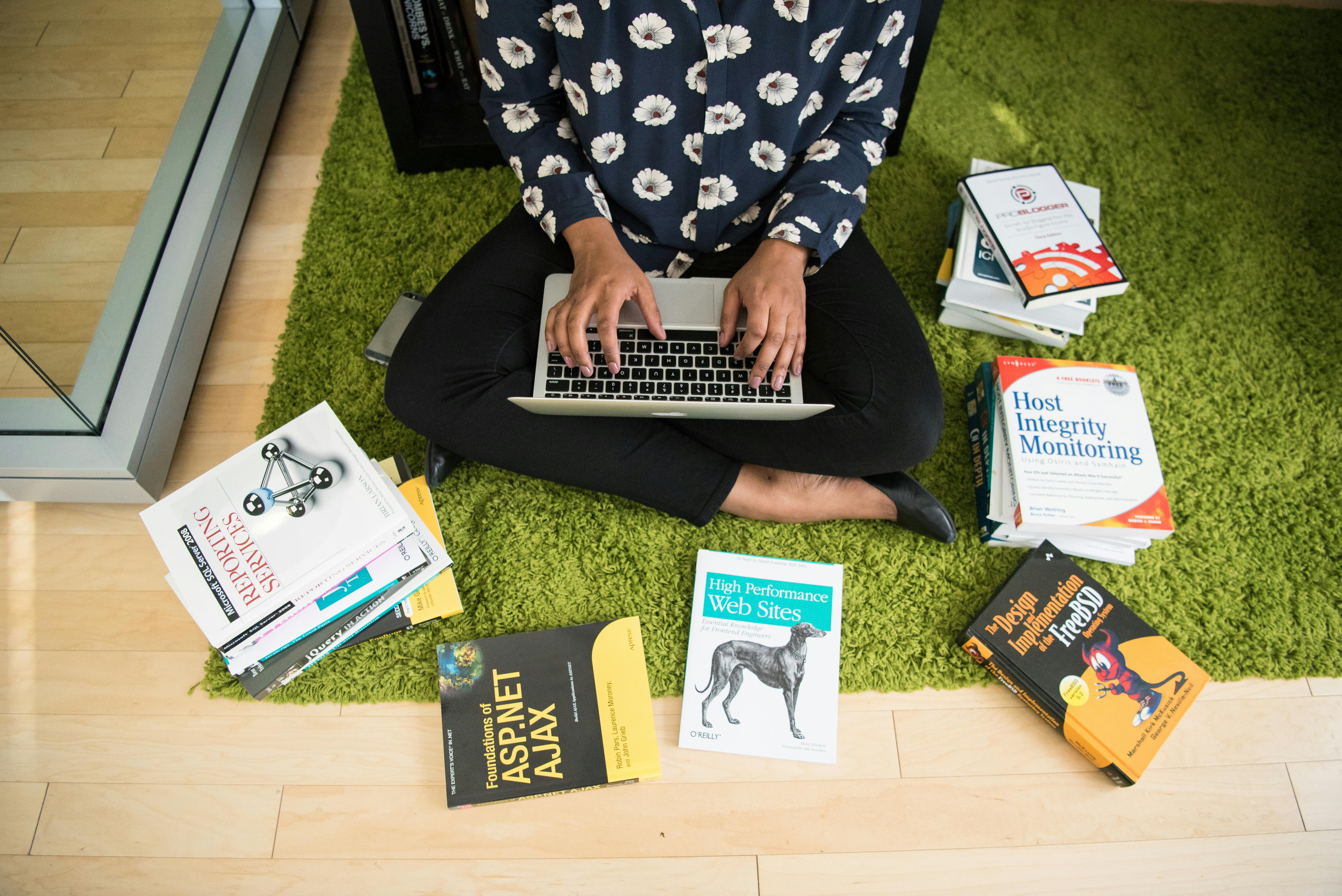 person with silver macbook on lap surrounded by books