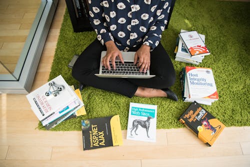 человек с серебристым Macbook на коленях в окружении книг