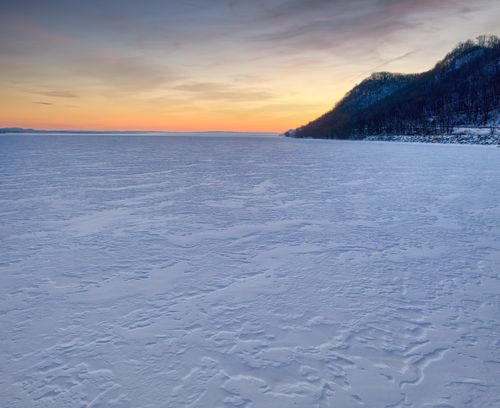 Free Serene winter sunset over a frozen lake in Minnesota showcasing icy textures and silhouetted hills. Stock Photo