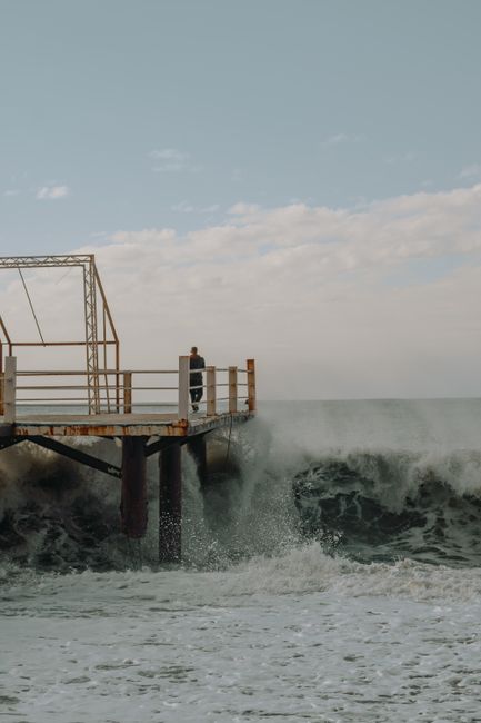 A solitary figure stands on a pier as powerful waves crash in Batumi, Georgia.