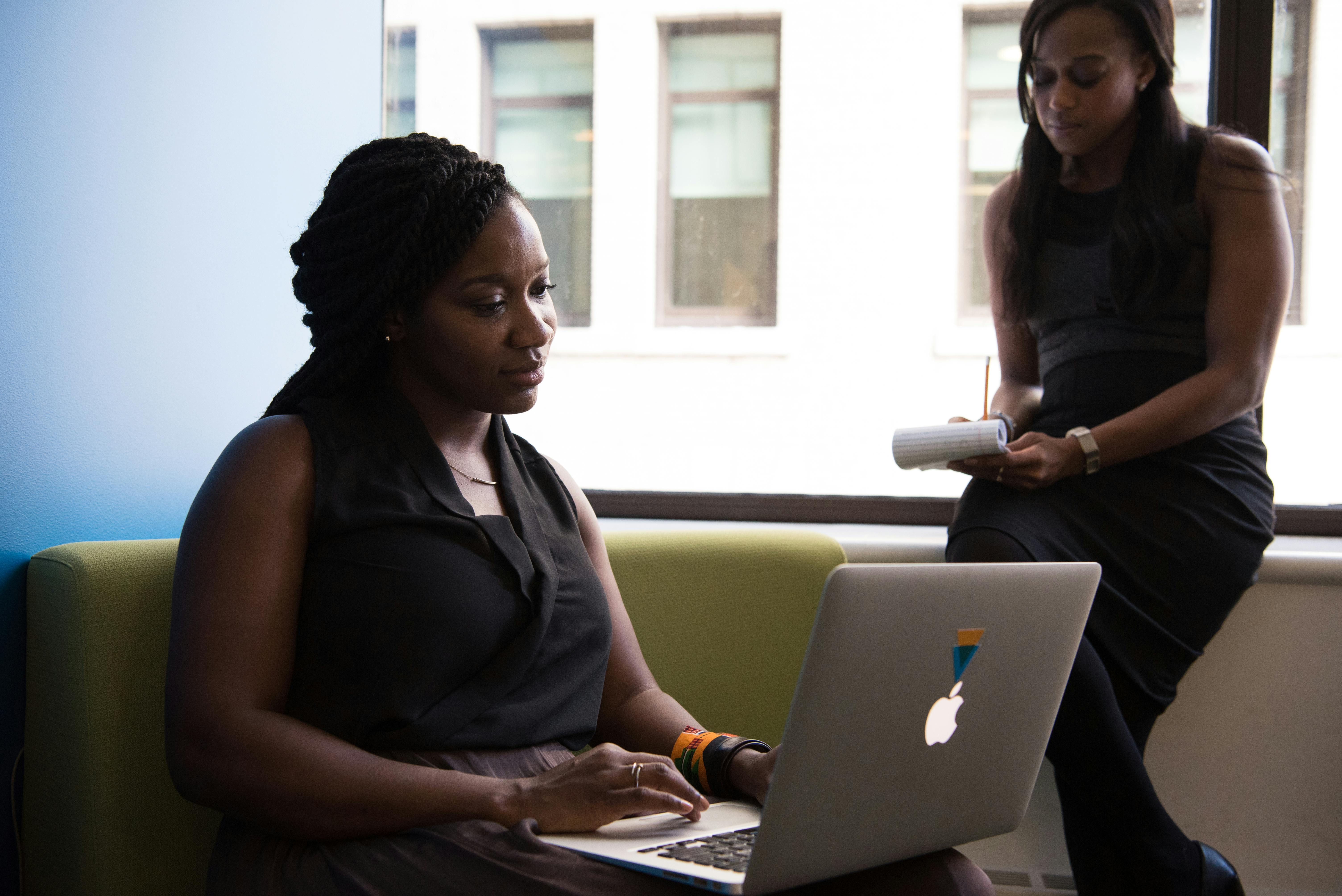 O poder do digital e da IA no empreendedorismo moderno 3 Two women in a business setting working on a laptop and taking notes, fostering teamwork.
