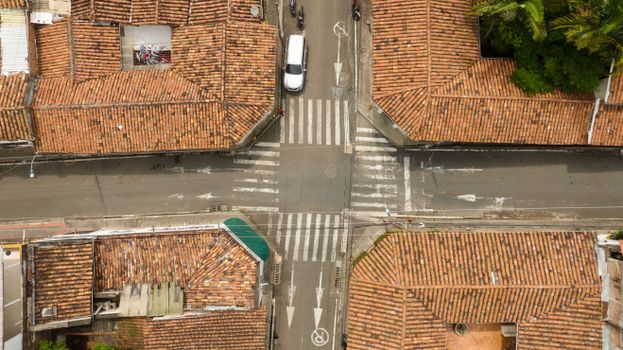 Aerial shot of an urban intersection with tile rooftops and a car below.