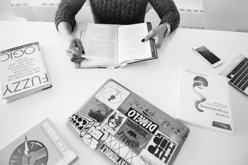 Grayscale Photo of Person Sitting Near Table With Books