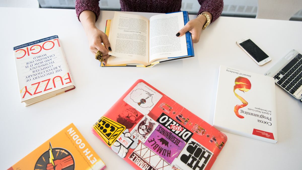 Overhead view of a workplace desk with books, a laptop, and technology essentials.