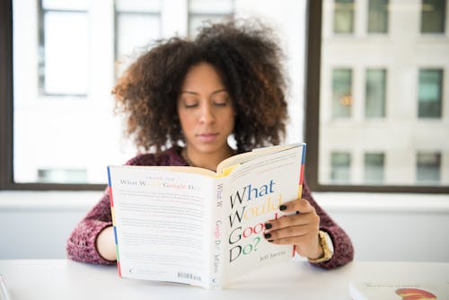 Sitting Woman While Reading Books Near Table