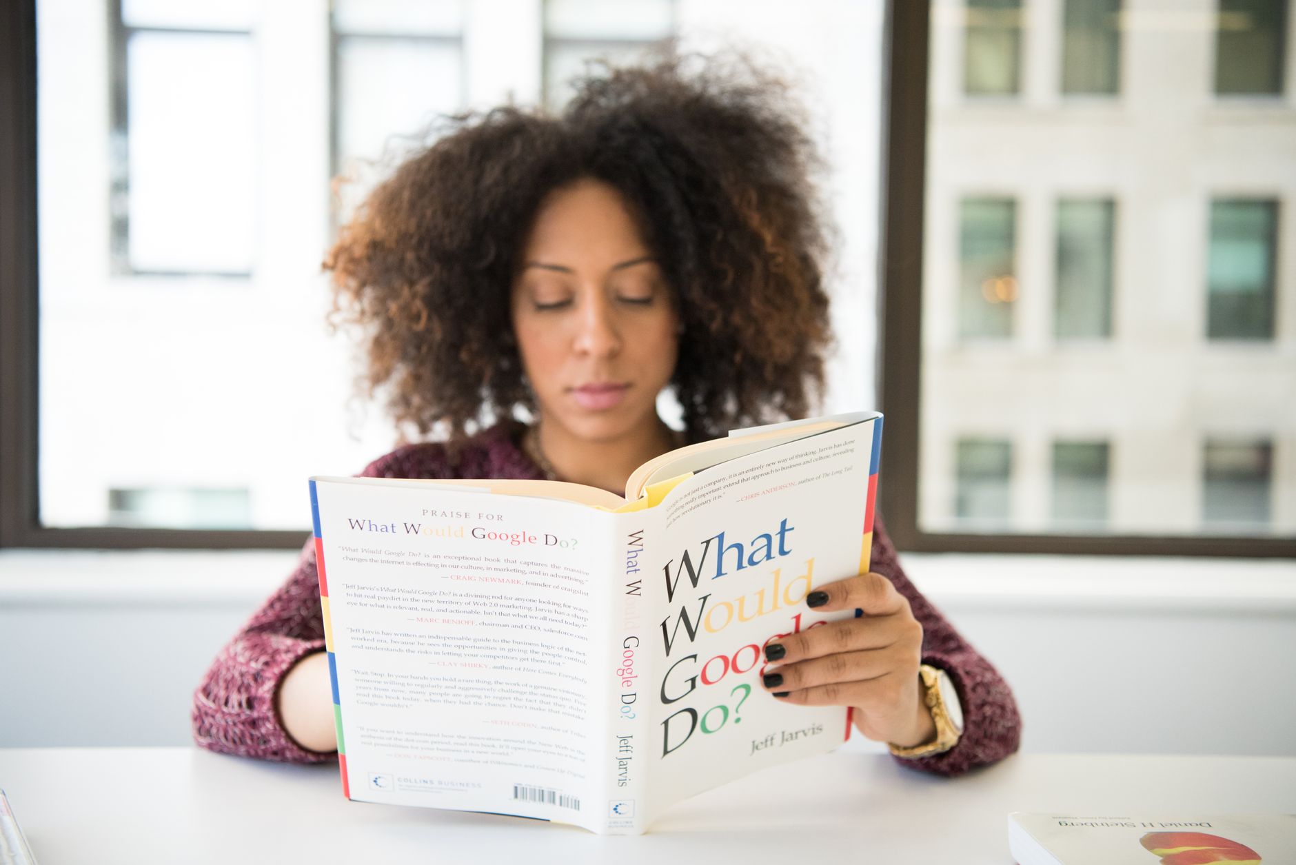 Focused woman reading a book indoors near a window, absorbing knowledge.