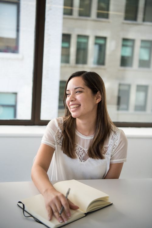 Free Woman enjoying writing in a notebook with natural daylight in modern office. Stock Photo