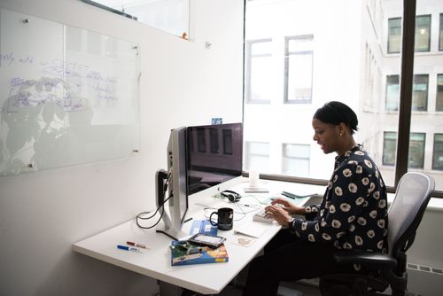 Free Woman sitting at a desk in a modern office, working on a desktop computer. Stock Photo