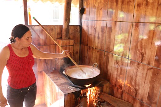 An adult woman stirring food in a pot over an open fire in a wooden interior kitchen. Rustic cooking setting.