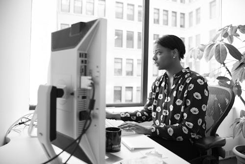 Gray Scale Photography of Woman Sitting on Armchair Facing Computer Monitor