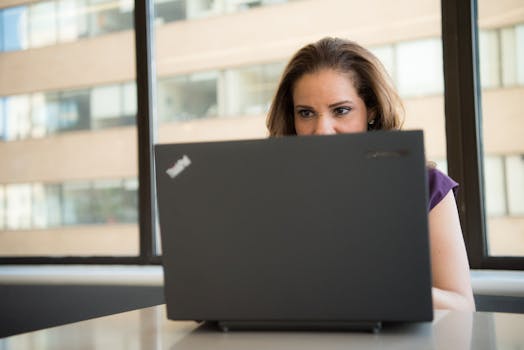 Focused woman using a laptop in a brightly lit office setting, showcasing modern work technology.