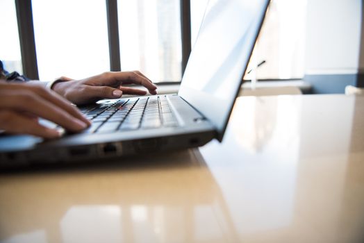 Close-up of woman's hands typing on a laptop in a bright, modern office environment.
