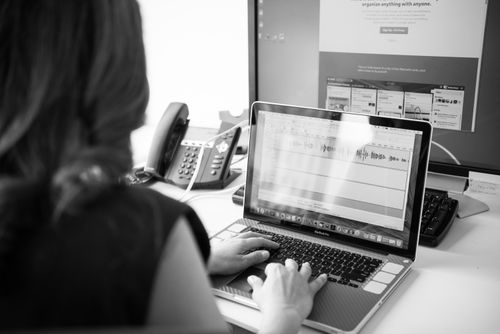 Free Black and white office scene with a woman working on a laptop in front of dual monitors. Stock Photo