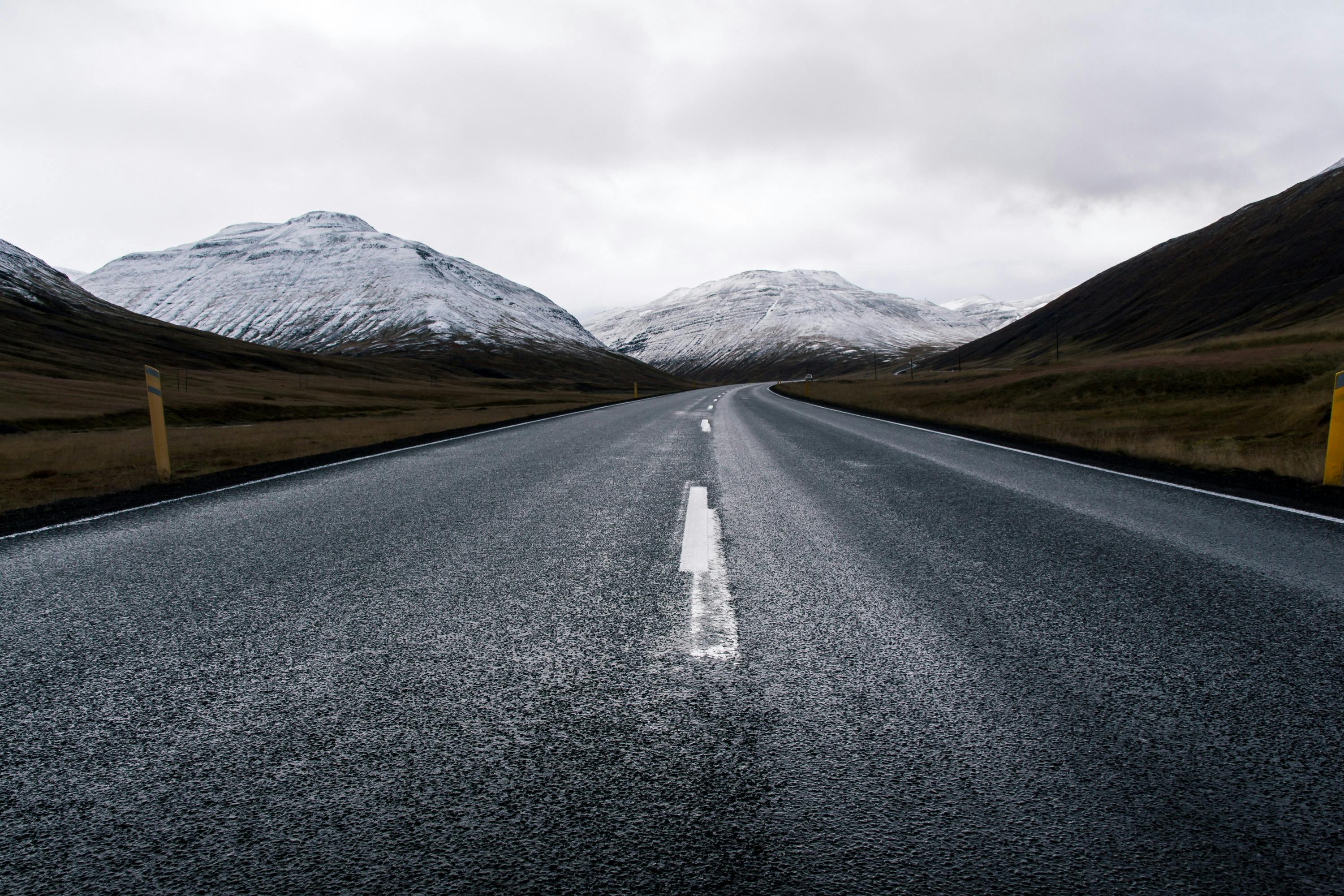 Prescription Goggle Inserts - A desolate highway stretches towards snow-capped mountains under a cloudy sky.