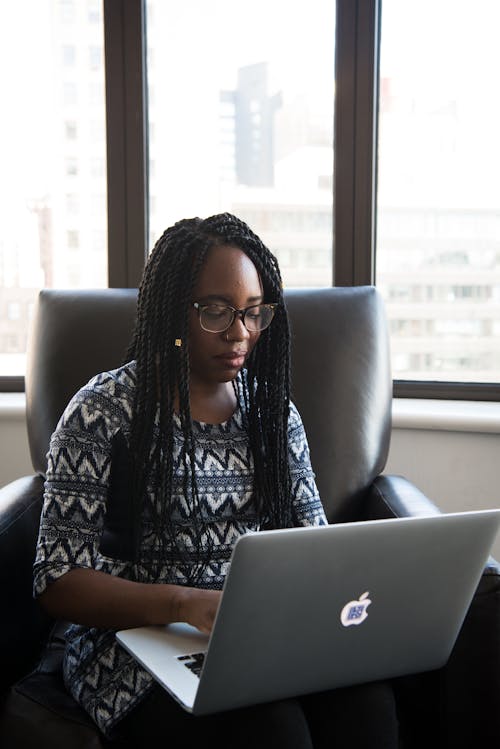 Woman in Black and White Blouse Sitting on Black Leather Chair Holding Her Laptop