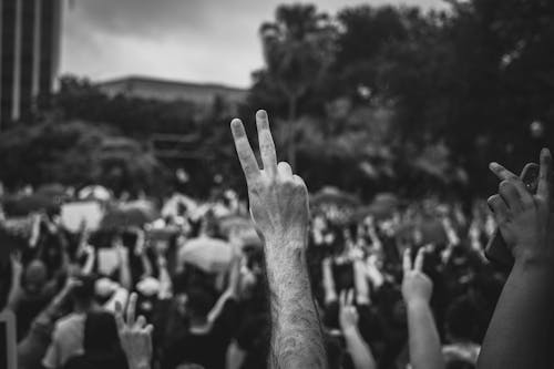 Grayscale Photo of People Raising Their Hands and Doing Peace Sign