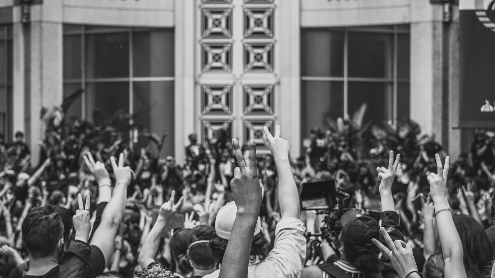 Crowd of activists raising peace signs near a City Hall during a rally.