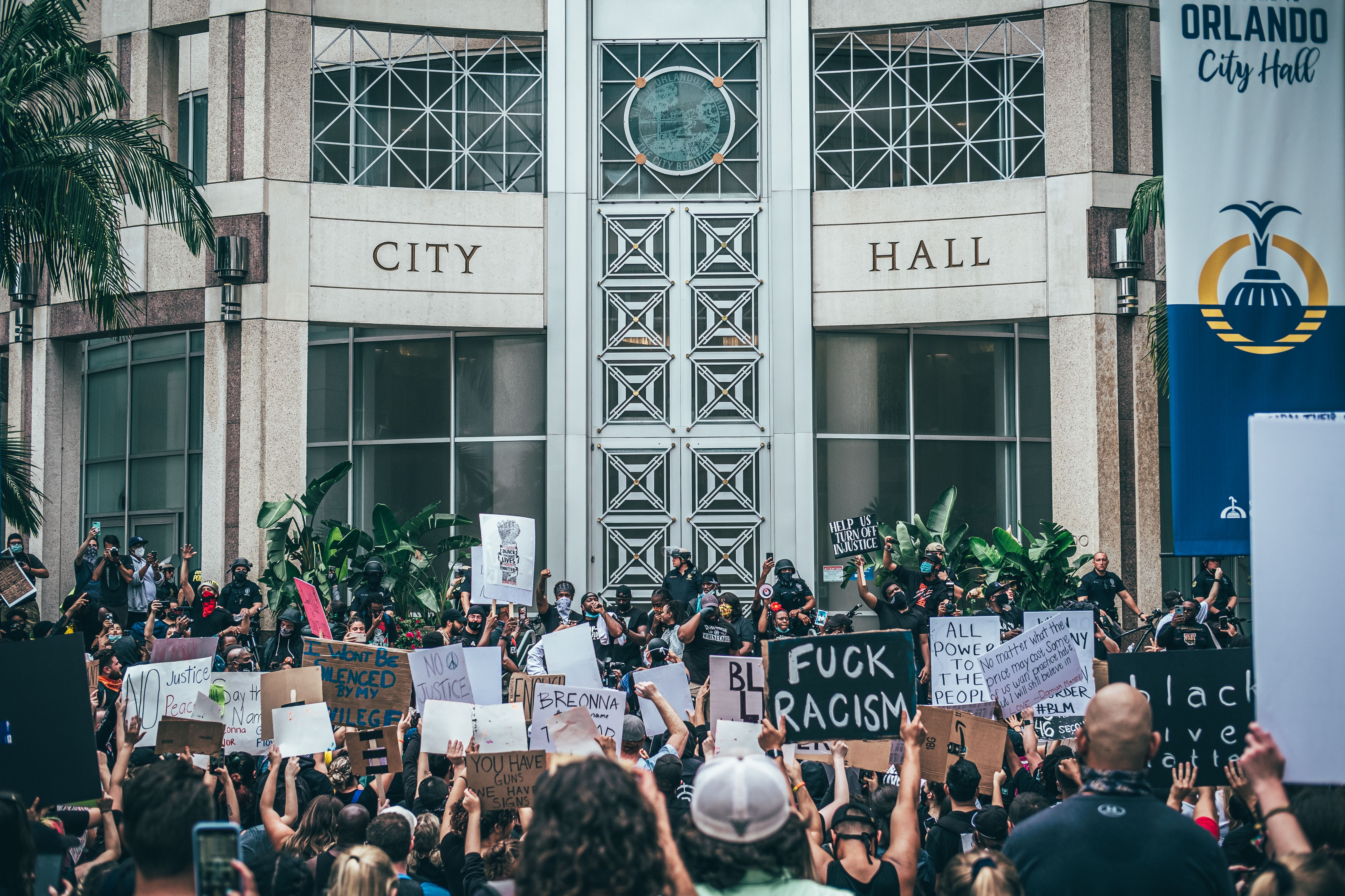 A large Black Lives Matter protest takes place outside Orlando City Hall with diverse participants holding signs.