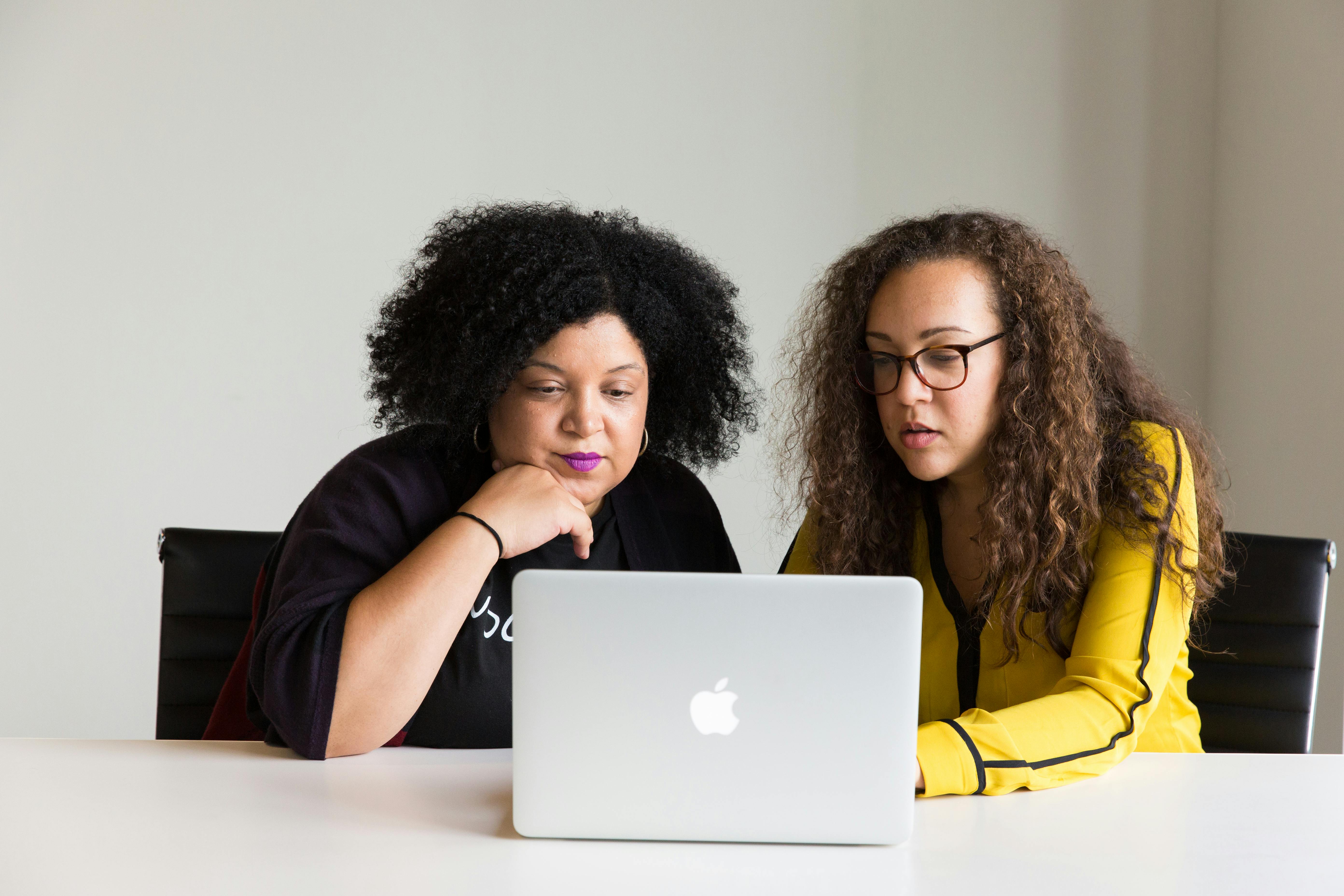 Two diverse women collaborating on a laptop in a modern office setting