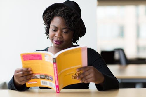 Woman in Black Long-sleeved Shirt Reading a Yellow Covered Book