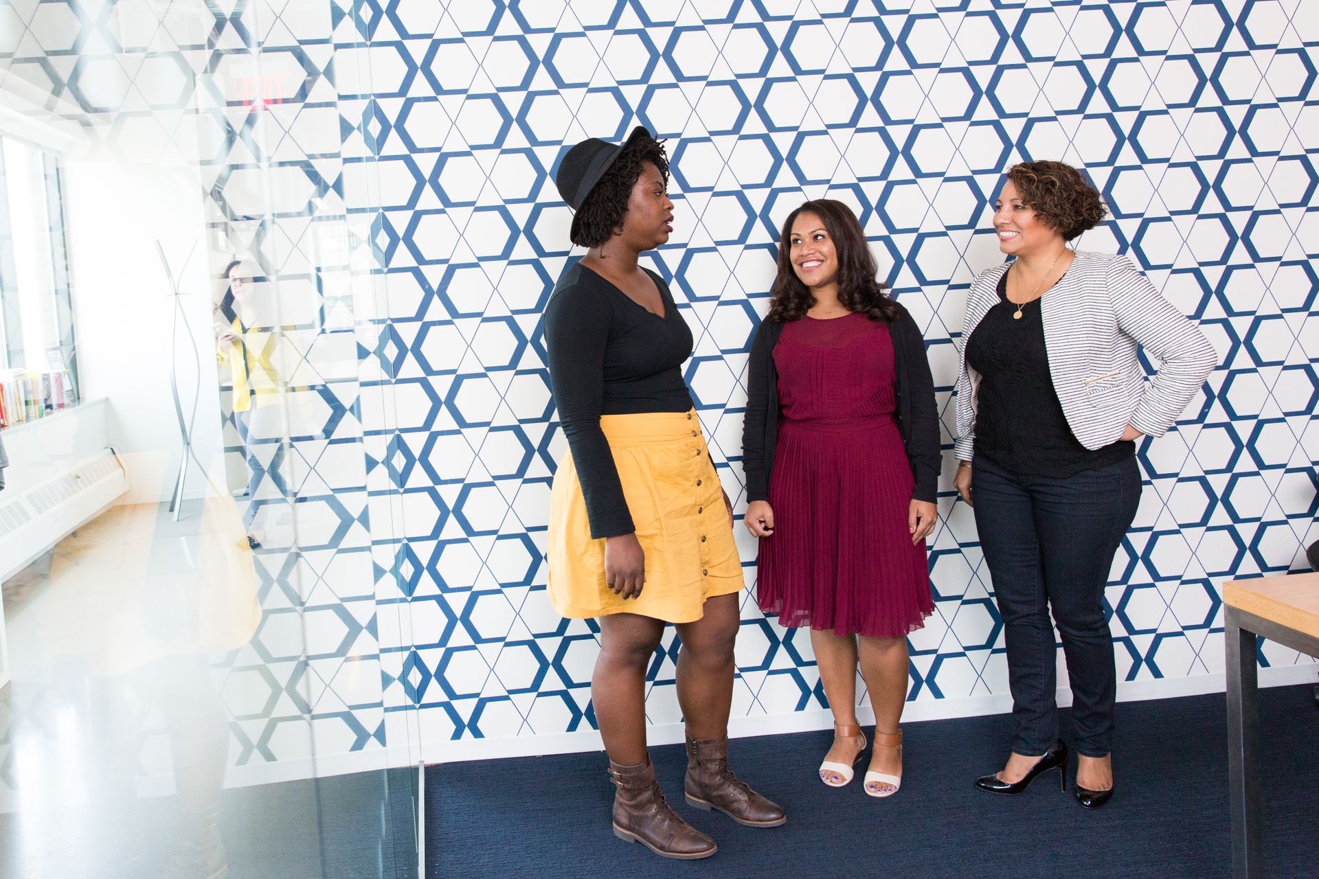 Group of women chatting in a stylish office with geometric patterns. Perfect for lifestyle and fashion themes.