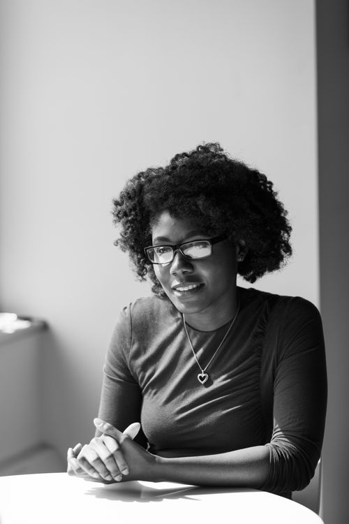 Free Captivating black and white photo of a smiling woman with curly hair and eyeglasses sitting indoors. Stock Photo