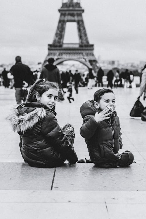 Grayscale Photo of Kids Sitting on Concrete Floor