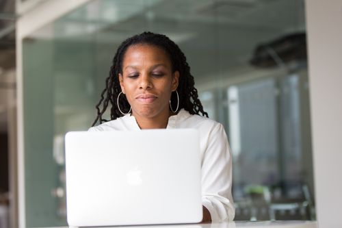 Free Focused African American woman working remotely on a laptop in a contemporary office setting. Stock Photo