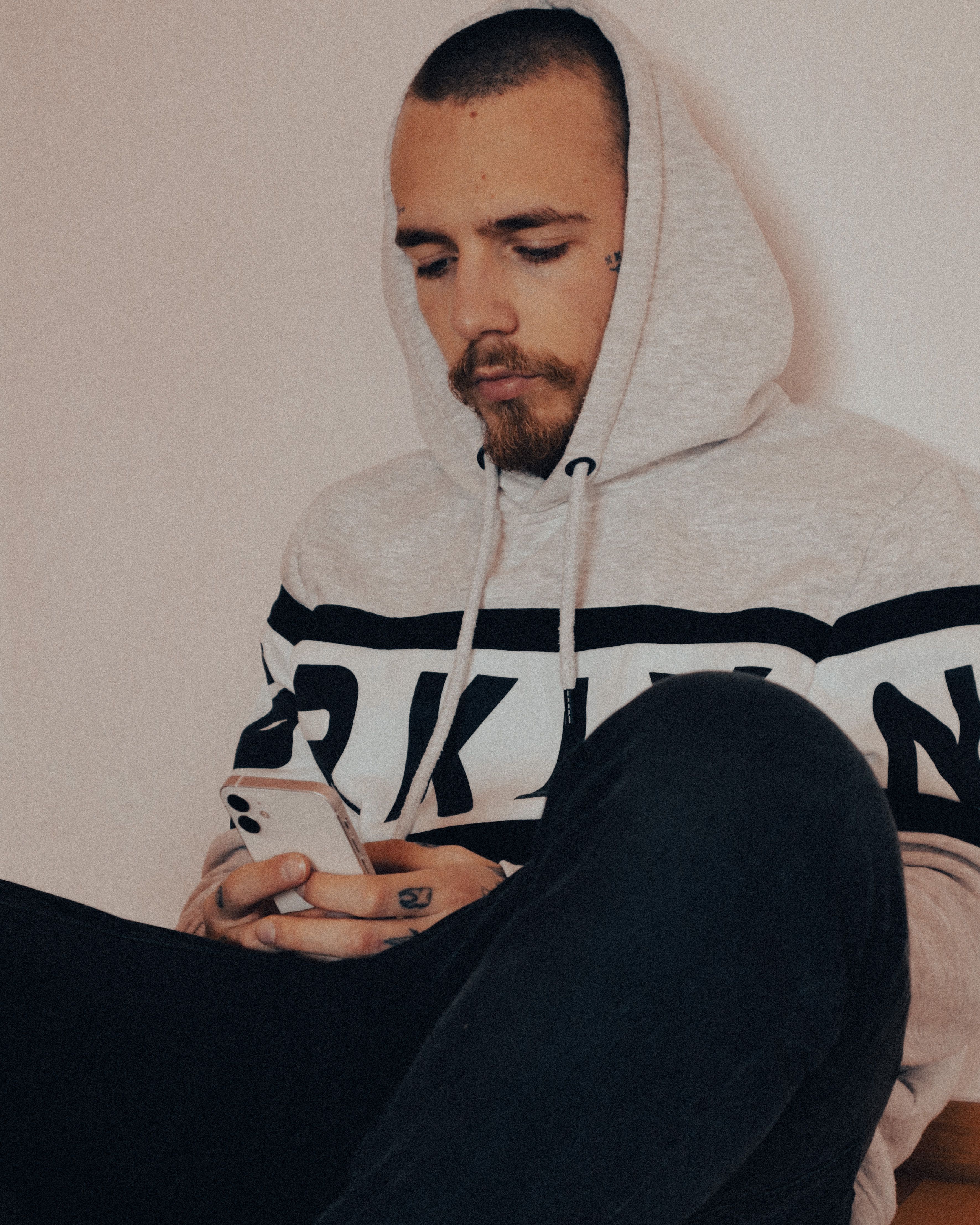 Young man in hoodie sitting indoors using smartphone in Bretten, Germany.