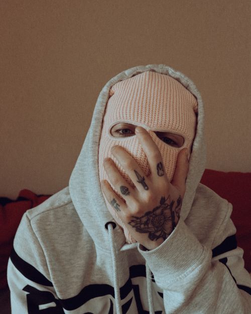 Free Portrait of a person in a hoodie and ski mask, showcasing hand tattoos, indoors. Stock Photo